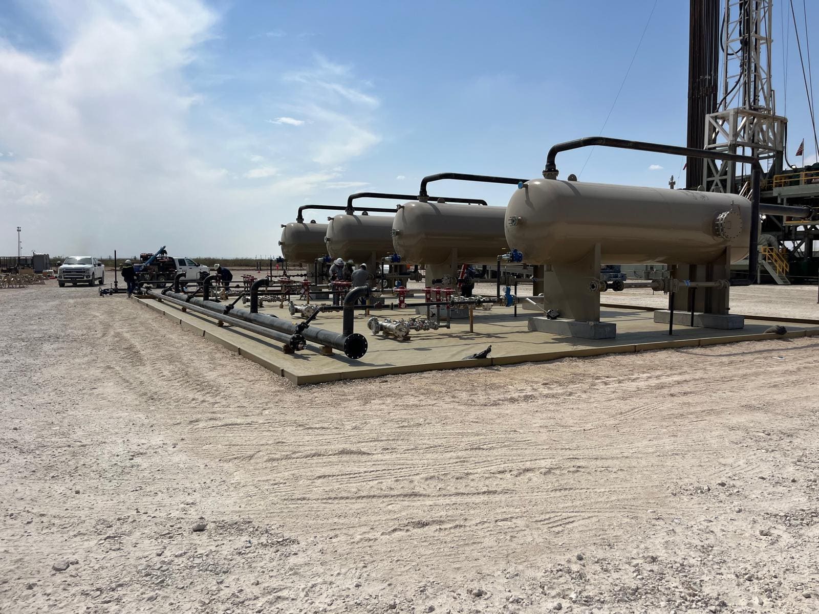 Four separator vessels set on a pad with a drilling rig behind them
